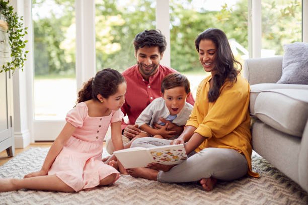 Family At Home Sitting On Floor In Lounge Reading Book Together